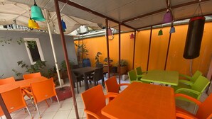 Ein Café mit orangefarbenen und grünen Tischen und Stühlen, einem Sandsack und Zimmerpflanzen.