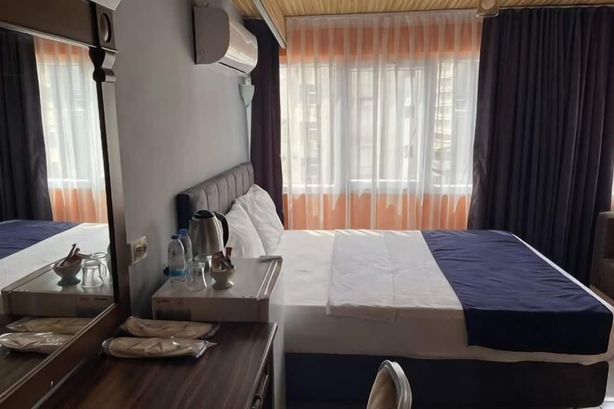 A hotel room with a bed, a desk with a mirror, a chair, and a window with curtains.