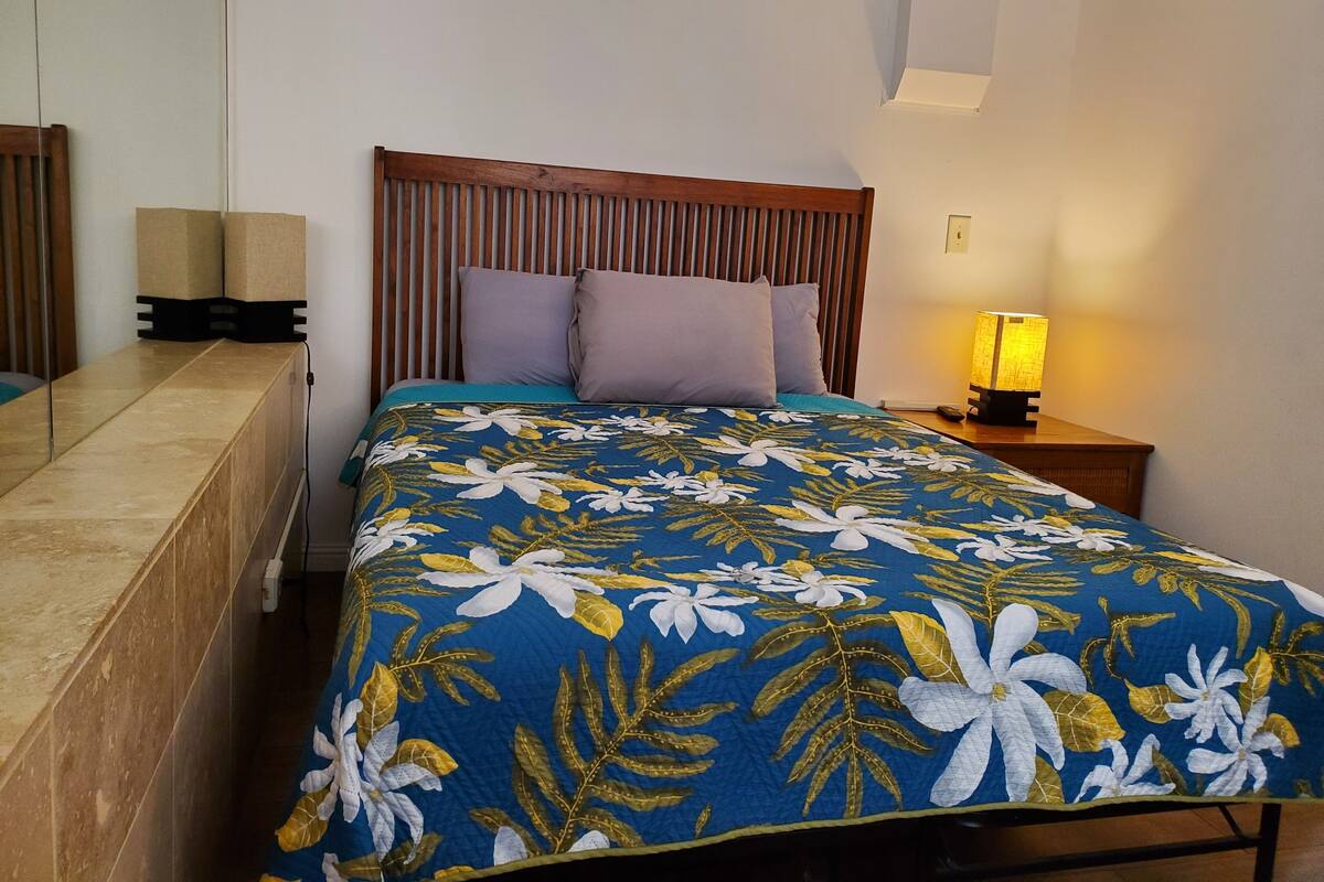 A neatly made bed with a floral bedspread, a wooden headboard, and a bedside lamp.