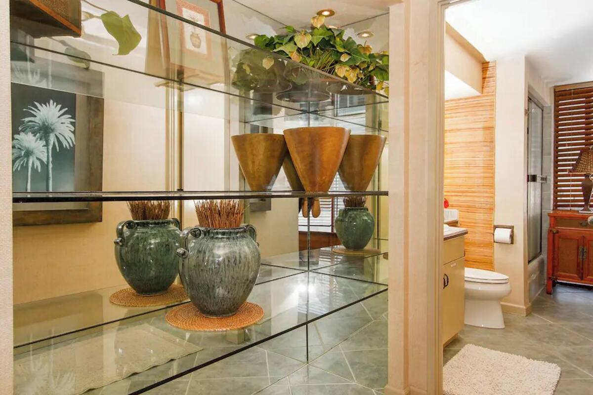 A modern bathroom with a glass shelf holding decorative vases, a toilet, and a wooden cabinet.