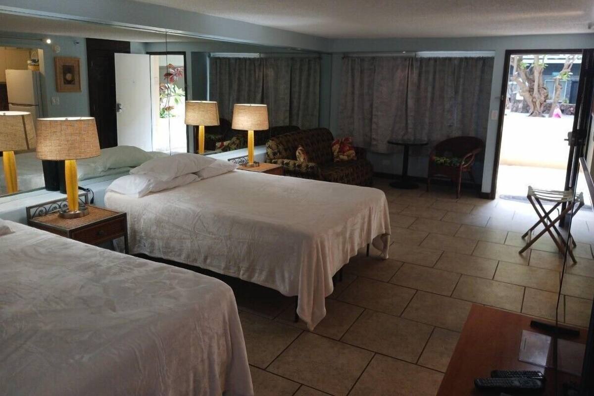 A hotel room with two beds, a sitting area with a chair, a small table, and a window with curtains.