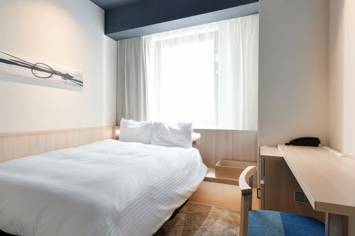 A hotel room with a bed, a desk, and a window with curtains.