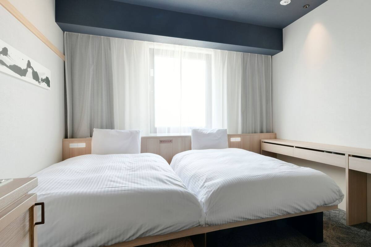 A modern hotel room with a double bed, a desk, and a large window with curtains.