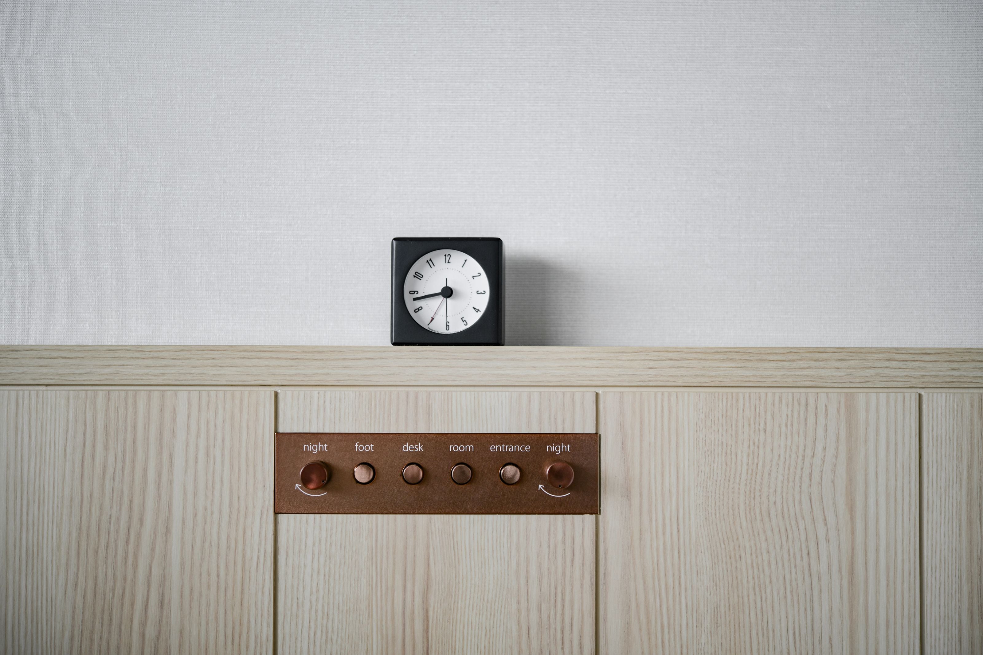 En väggklocka och en kontrollpanel med knappar märkta med orden ”natt”, ”fot”, ”skrivbord”, ”rum”, ”ingång” och ”natt”.