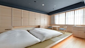 Een moderne slaapkamer met twee bedden, een klein tafeltje, stoelen en grote ramen die natuurlijk licht binnenlaten.