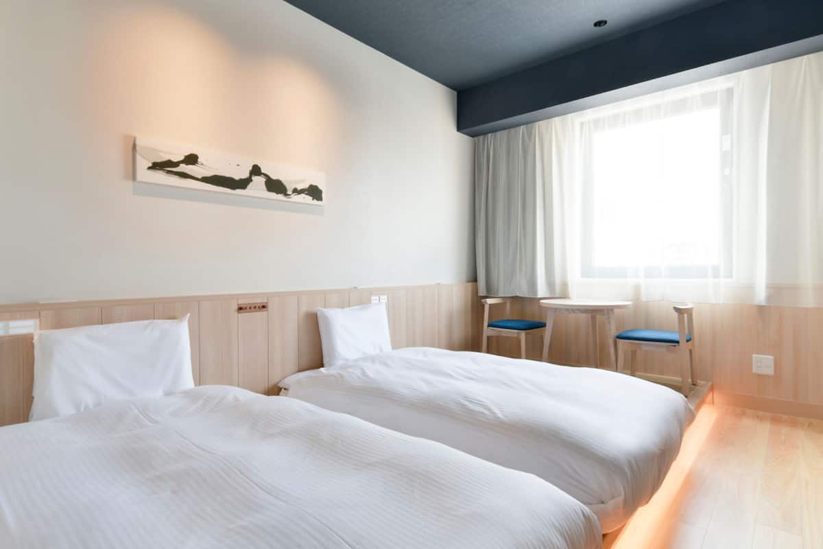 A hotel room with two beds, a small table, and a chair.