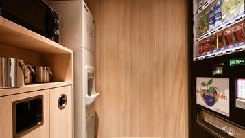 Cocina compacta con microondas, hervidor y dispensador de agua. Hay un estante con ollas de acero inoxidable y una ventana pequeña.