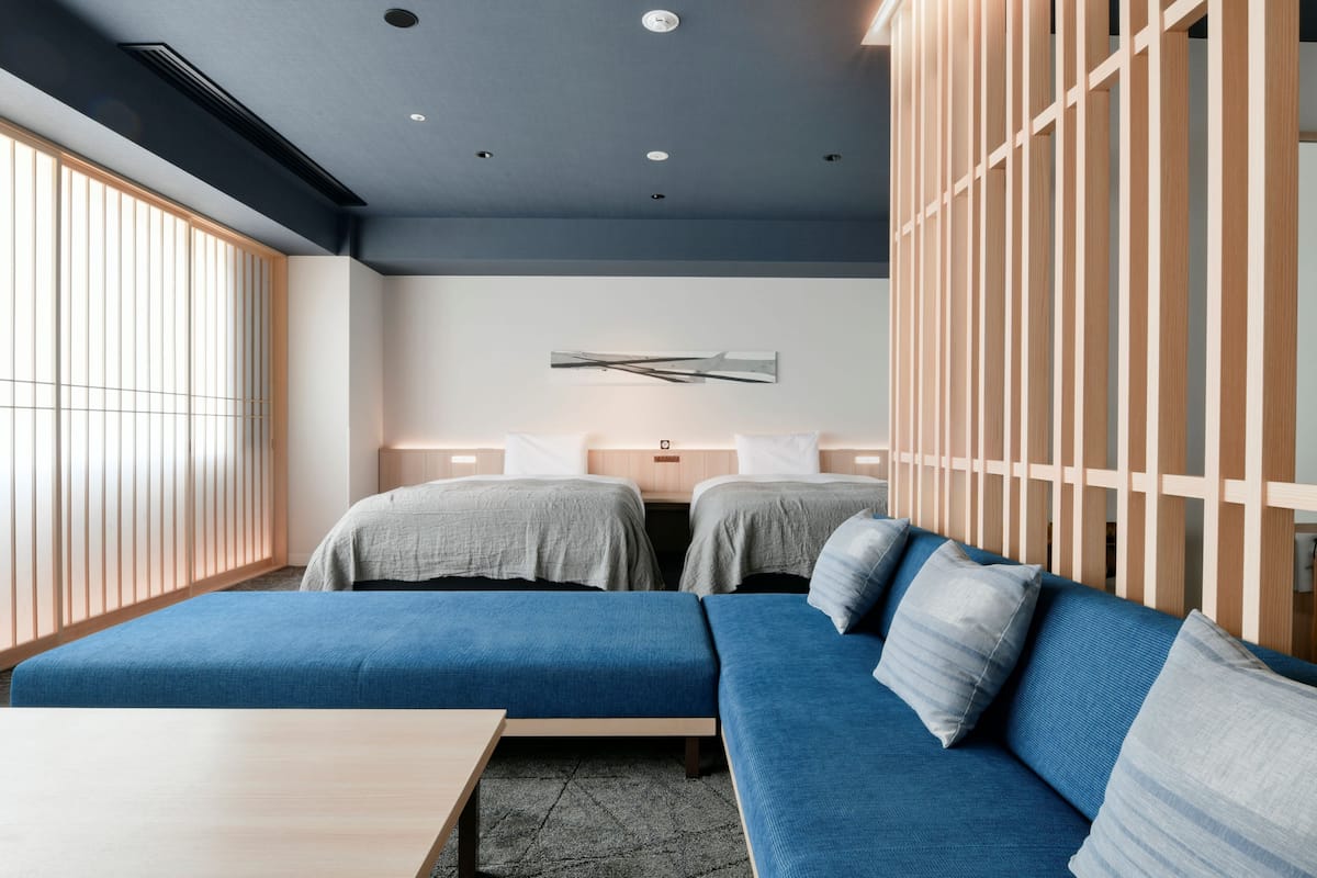 A modern hotel room with two beds, a sofa, a wooden partition, and a wall-mounted artwork.
