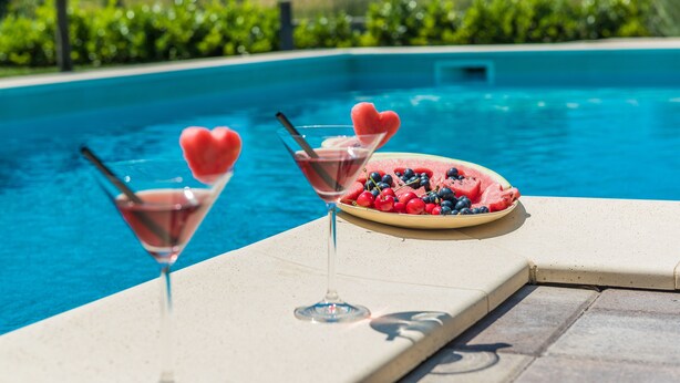 Een zwembadterras met twee martini-glazen en een schaal watermeloen en bessen.