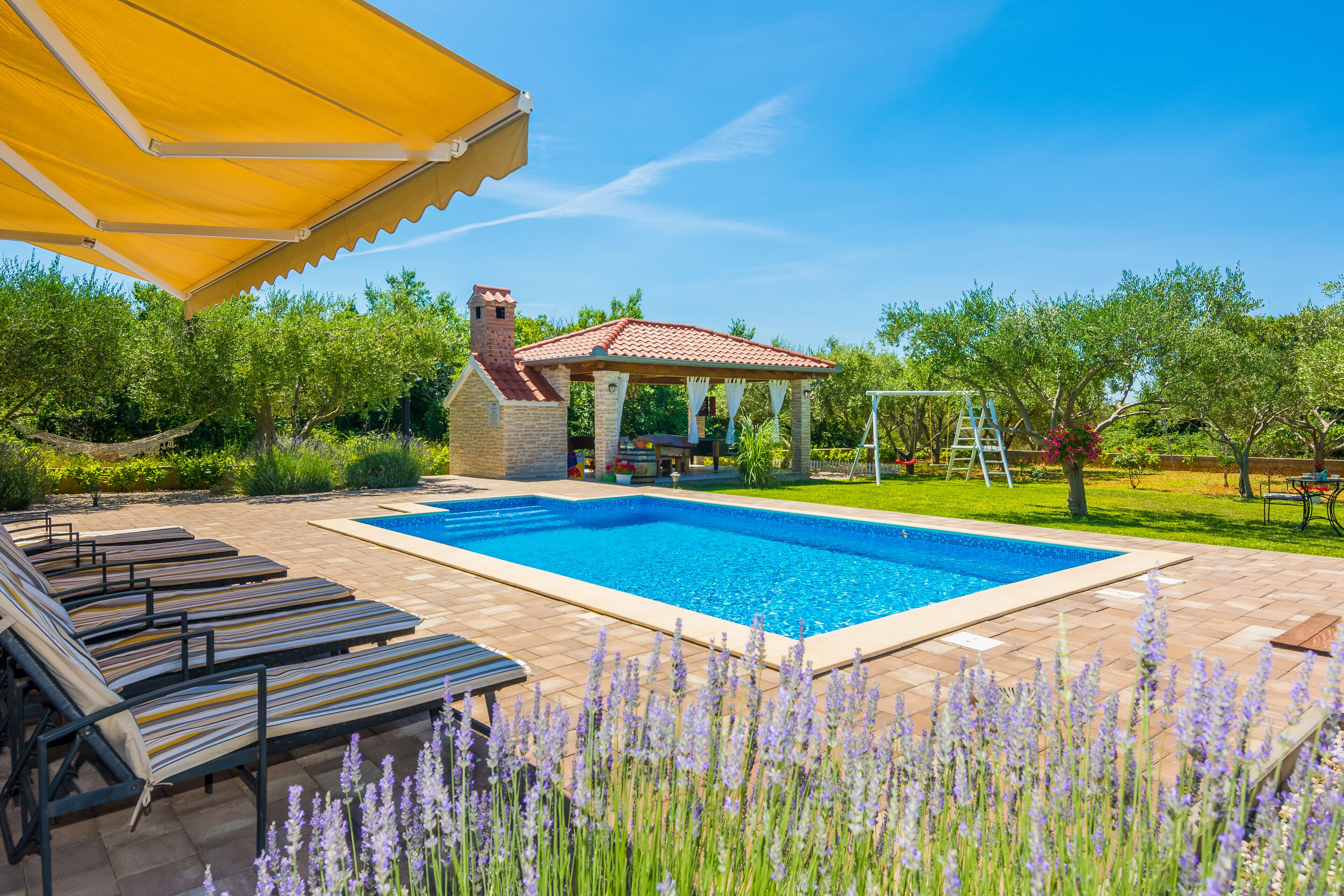 A swimming pool with lounge chairs, a gazebo, and a garden with lavender plants.