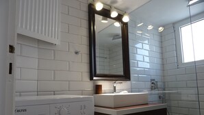 A modern bathroom with white tiled walls, a built-in washing machine, a sink with a mirror above it, and a window providing natural light. - Minimal Luxury near Acropolis (Athens)