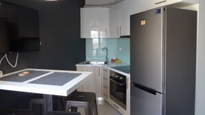 A modern kitchen with white cabinets, a stainless steel refrigerator, a built-in oven, and a dining area with stools. - Minimal Luxury near Acropolis (Athens)