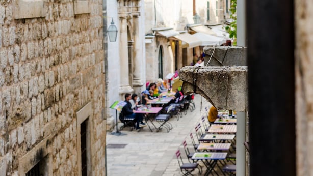 Une rue étroite bordée d’immeubles en pierre, avec des terrasses et des tables installées pour les repas.