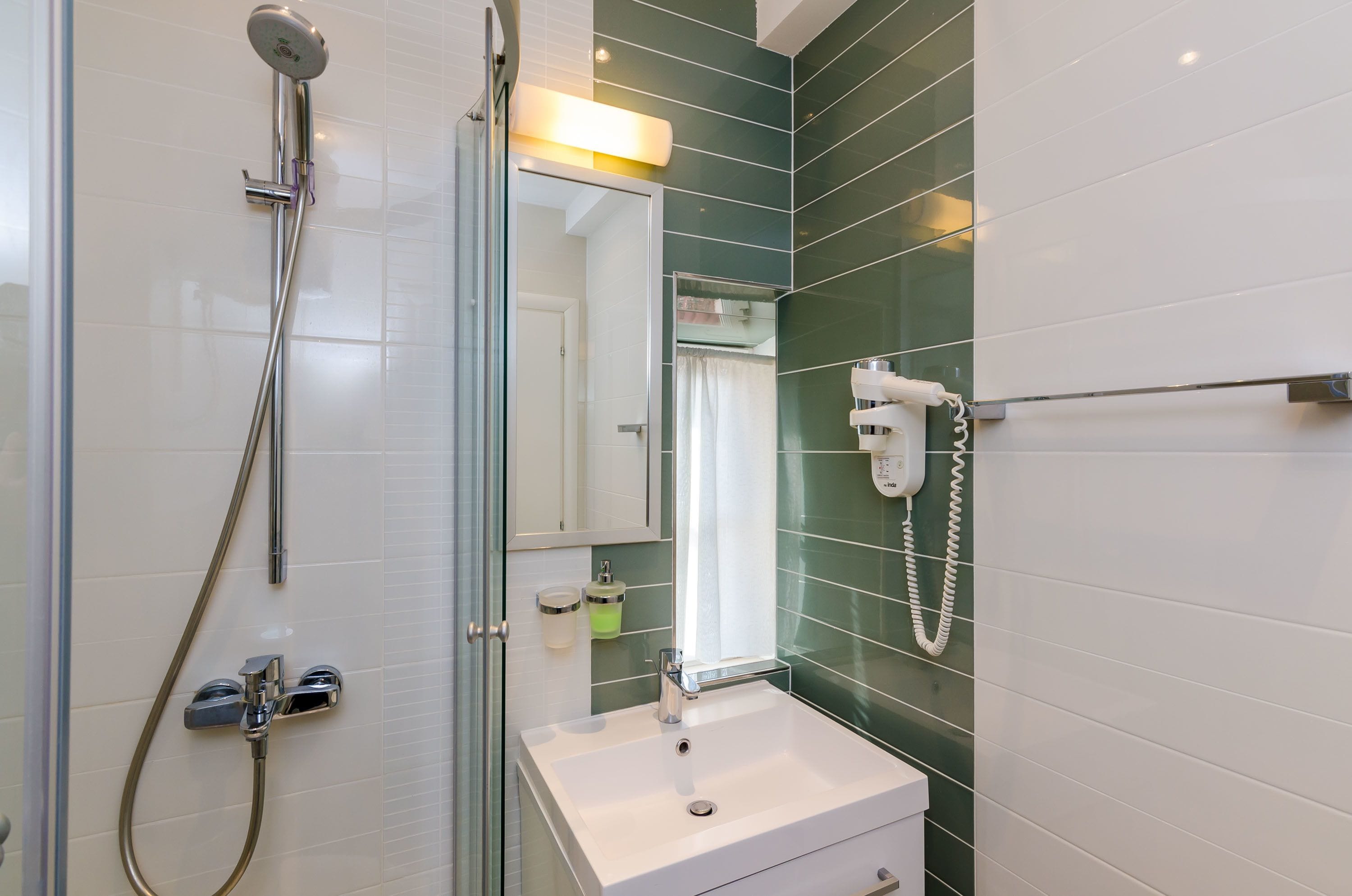 A bathroom with a glass shower enclosure, a white sink, a mirror, and a towel rack.