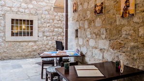 Une pièce aux murs de pierre, avec une table où sont exposées des œuvres d’art, une fenêtre grillagée et une chaise.