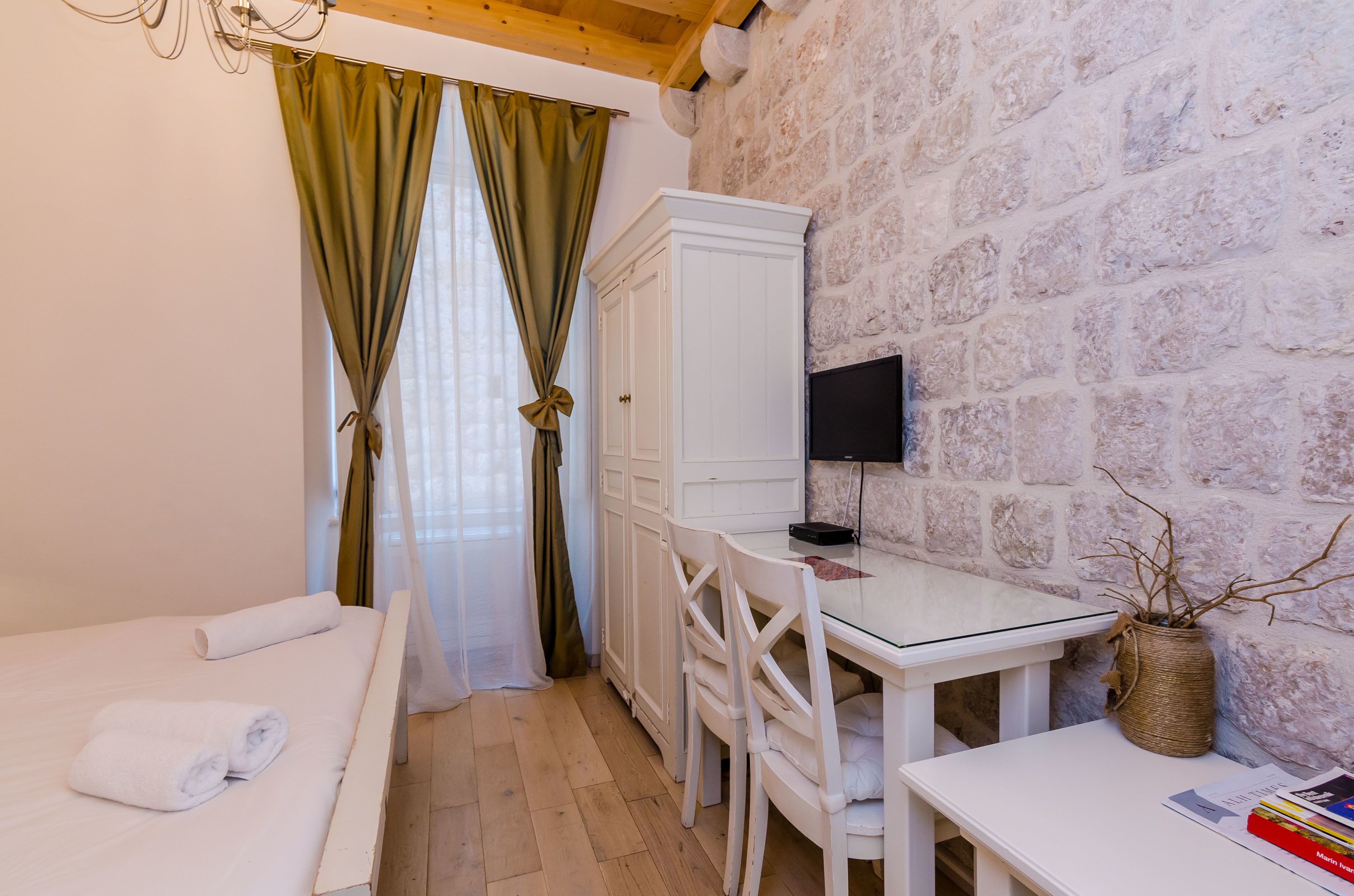 A bedroom with a bed, a desk, a chair, a television, and a stone wall.