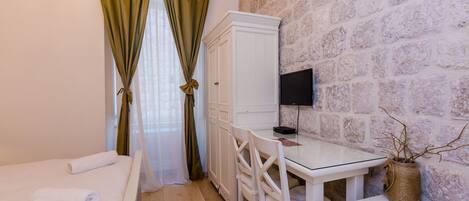 A bedroom with a bed, a desk, a chair, a television, and a stone wall.