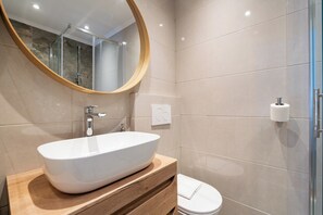 A modern bathroom with a large oval sink, a wooden vanity, a toilet, and a glass shower enclosure. - Cinema View House (Dubrovnik)