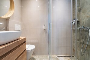 A modern bathroom with a glass-enclosed shower, a wooden vanity with a white sink, and a toilet. - Cinema View House (Dubrovnik)