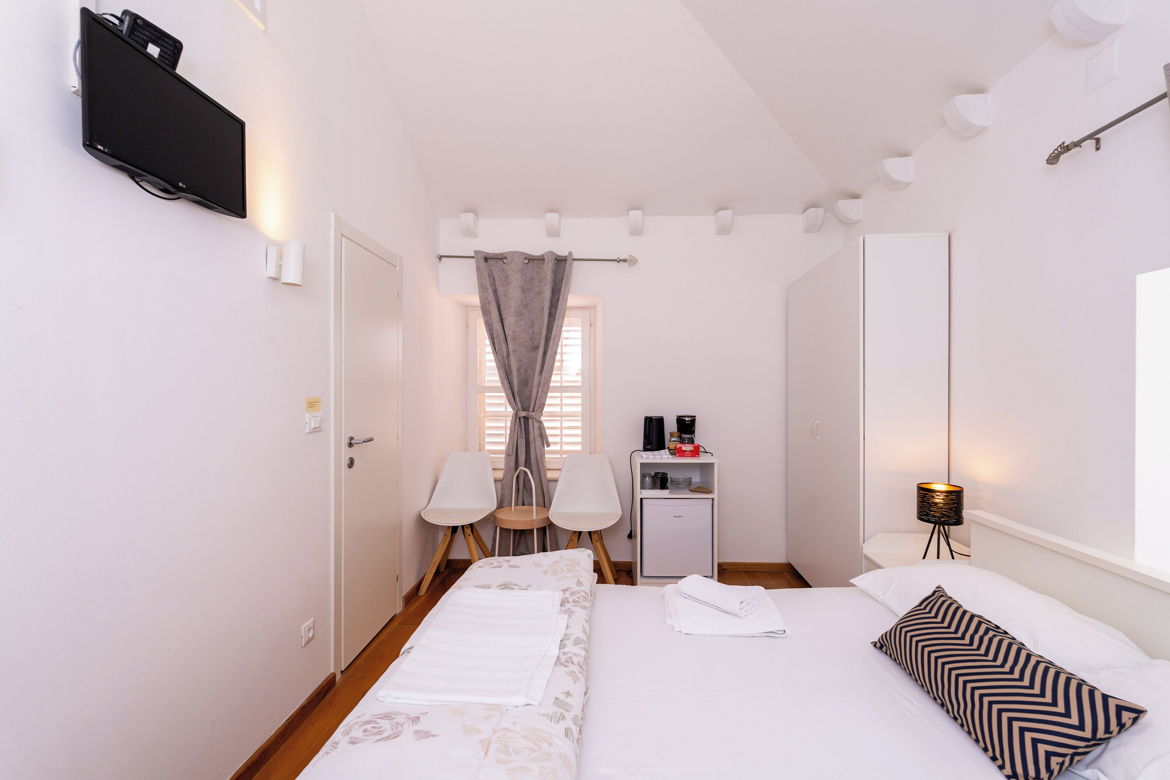 A hotel room with a bed, a desk with a lamp, a TV, and a window with curtains.