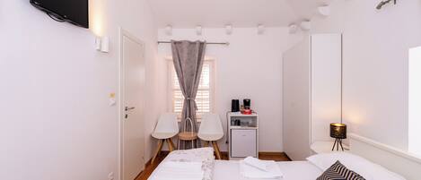 A hotel room with a bed, a desk with a lamp, a TV, and a window with curtains.