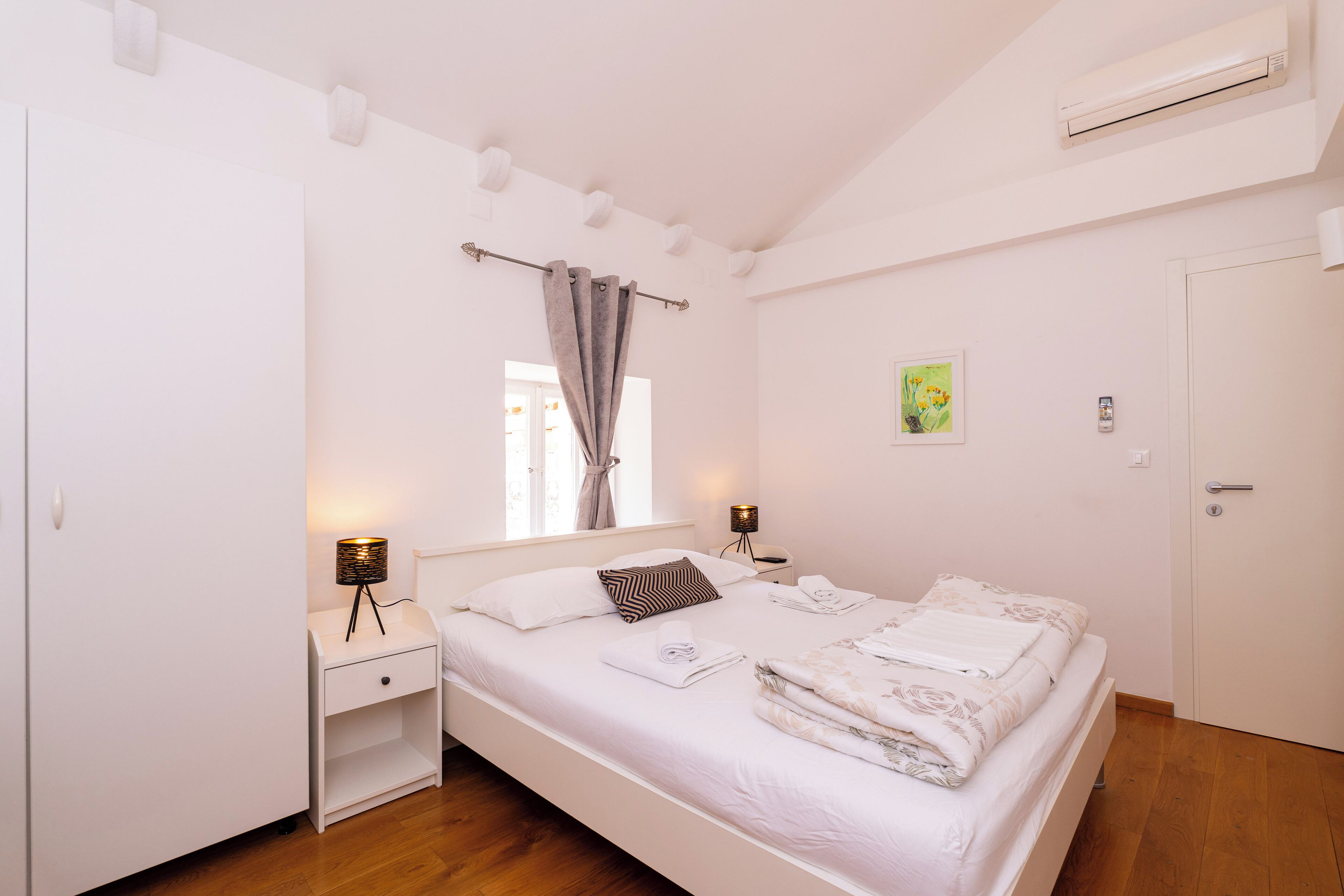 Een keurig opgemaakt slaapkamer met een bed, nachtkastjes, een kledingkast en een raam met gordijnen.
