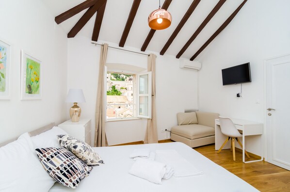 A bedroom with a bed, a desk, a chair, a TV, and a window with curtains. - Cinema View House (Dubrovnik)