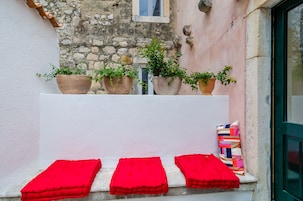 Pared de pedra com uma janela, plantas em vasos e almofadas vermelhas em um parapeito.
