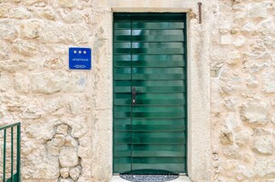 Um edifício de pedra com porta verde, uma placa azul indicando ser um apartamento e o número '12' na parede.