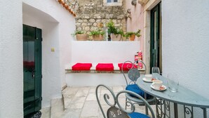 Un pequeño patio al aire libre con una mesa, sillas, plantas en macetas y un banco rojo.