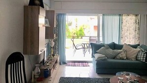 Uma sala de estar com sofá, uma poltrona, uma mesa e varanda com vista para o verde.