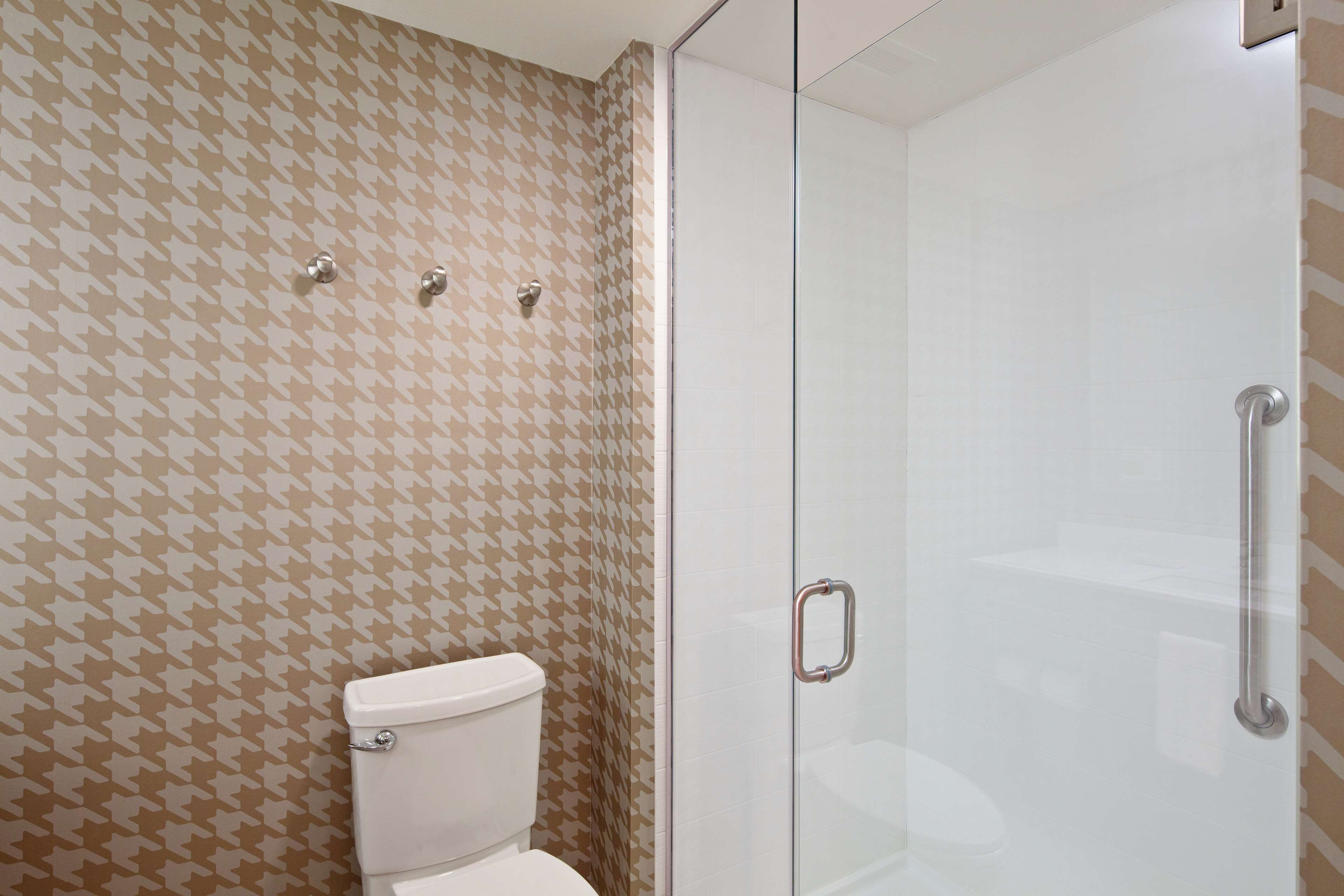 A bathroom with a patterned wall, a toilet, and a glass shower enclosure.
