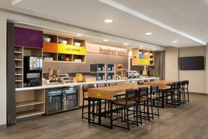 A modern kitchen area with a long counter, multiple appliances, and a dining table with chairs. - Home2 Suites by Hilton Alameda Oakland Airport (Alameda)