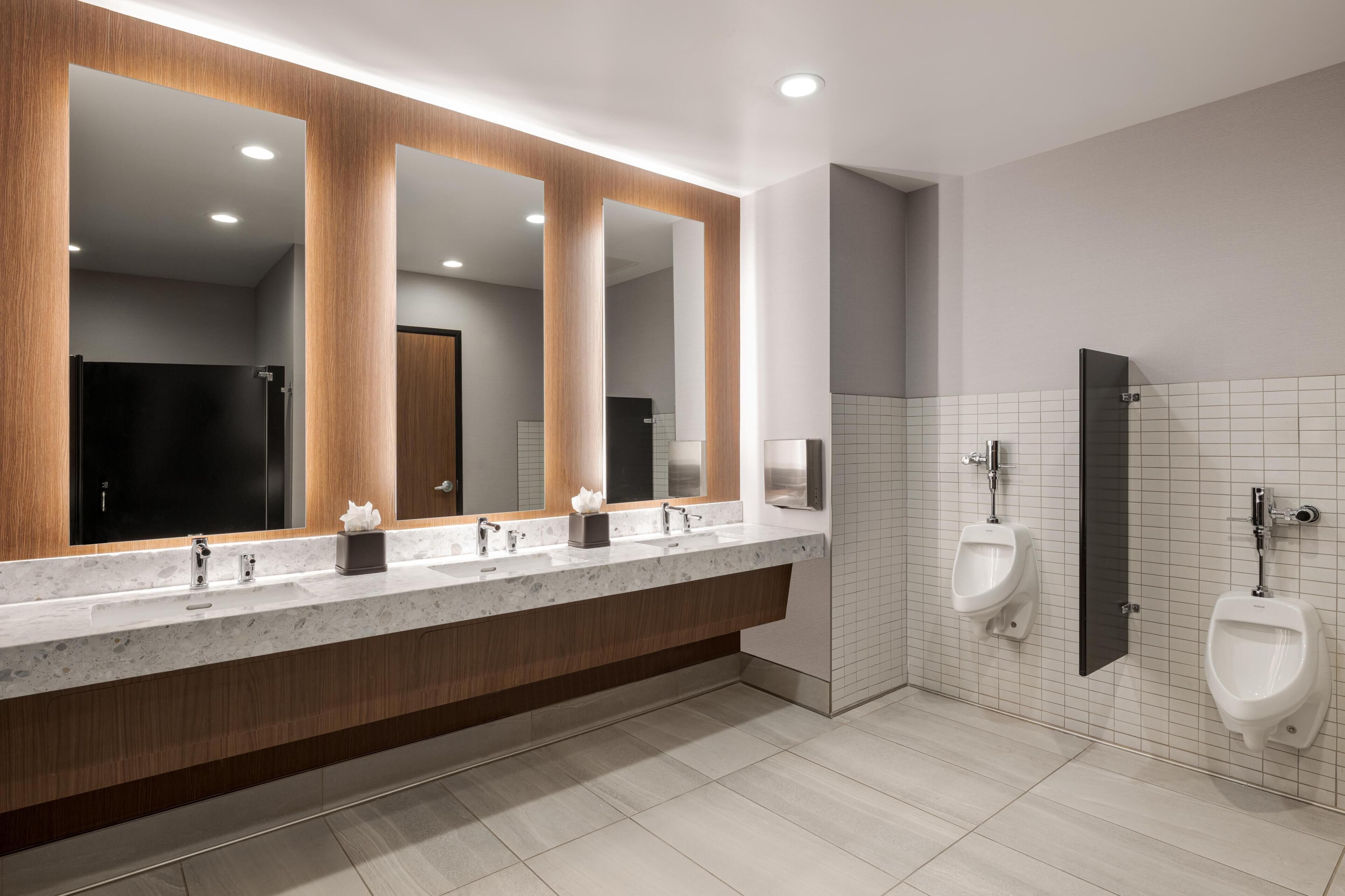 A modern bathroom with a large mirror, two sinks, and a urinal.