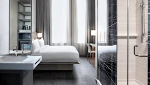 Una habitación de hotel moderna con cama, mesita de noche, lámpara y zona de ducha.