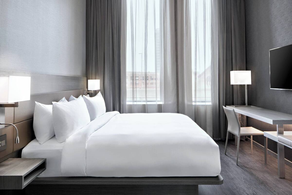 A modern hotel room with a large bed, bedside tables, a desk, and a TV.