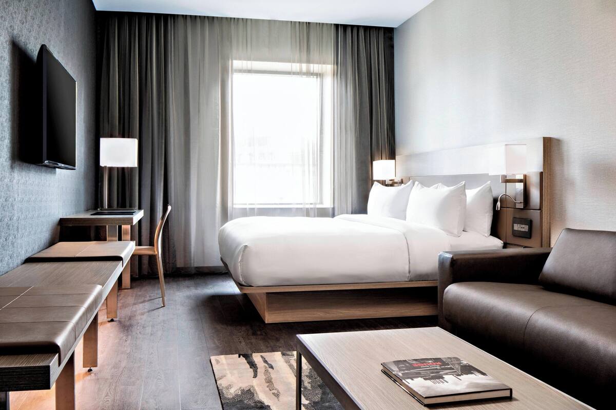 A modern hotel room with a bed, a sofa, a desk, and a television.