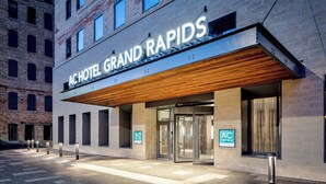 Exterior del hotel Grand Rapids con fachada moderna, un alero de madera y un edificio de ladrillo al fondo.