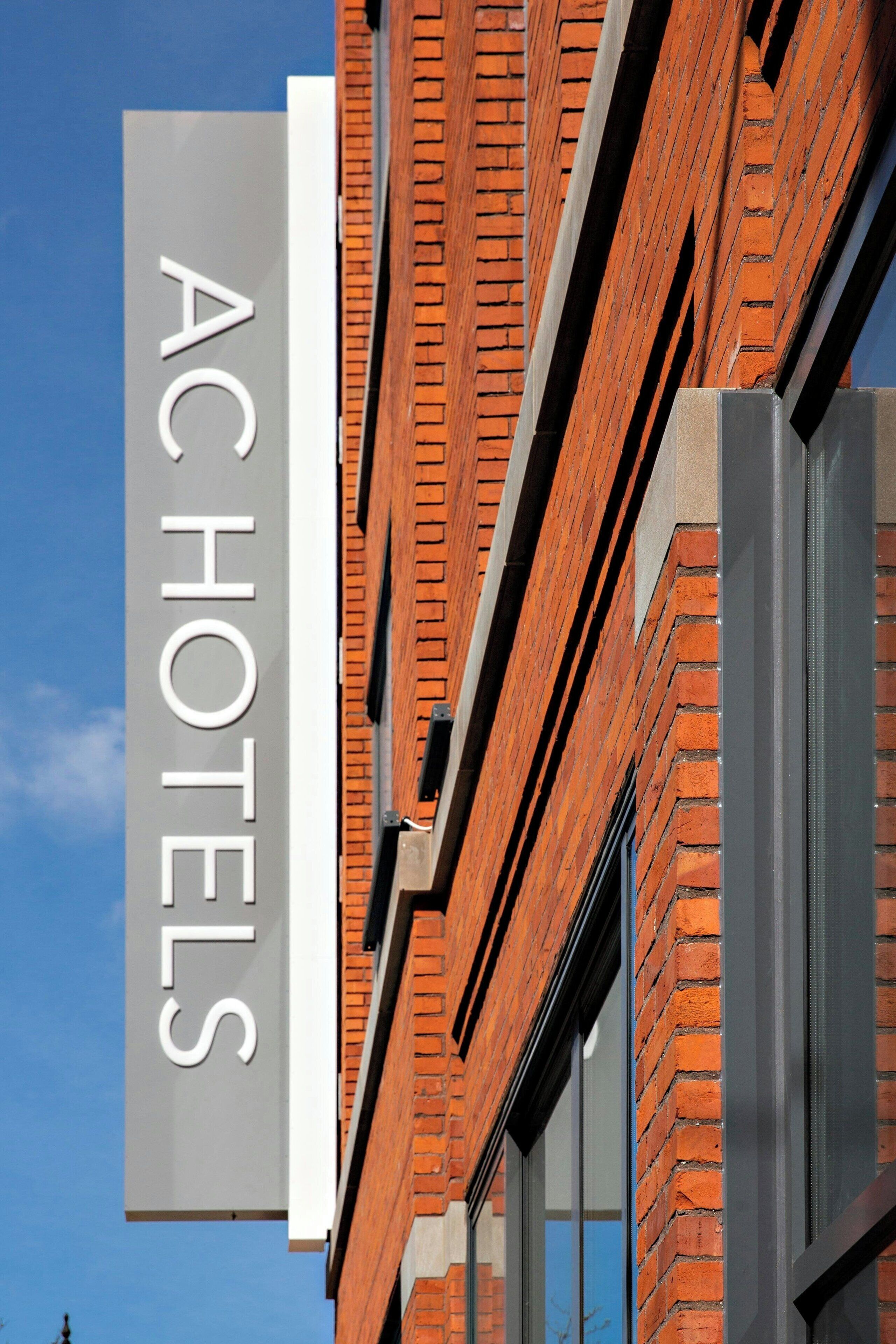 A hotel sign with the name "AC HOTELS" against a brick wall backdrop.