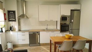 Une cuisine moderne avec des meubles blancs, des appareils en acier inoxydable et une table à manger en bois, accompagnée de chaises.