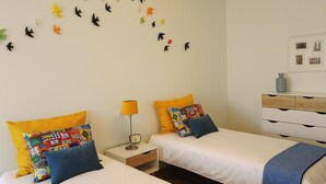 Une chambre d’hôtel avec deux lits, une table de chevet avec une lampe, une commode et un mur décoré d’autocollants représentant des oiseaux.