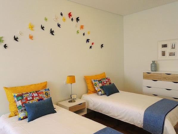 A hotel room with two beds, a nightstand with a lamp, a dresser, and a wall decorated with bird decals.