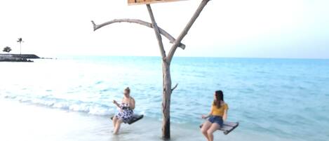 A beach scene with a wooden sign that reads "I ♥ GAAFARU" and two people enjoying the water.