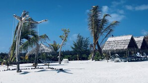 A beach resort with thatched-roof huts, palm trees, and lounge chairs.