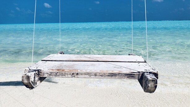 A wooden swing chair suspended over clear turquoise water.