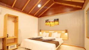 A bedroom with a wooden ceiling, a bed with white bedding, a wooden headboard, and a wall-mounted painting.