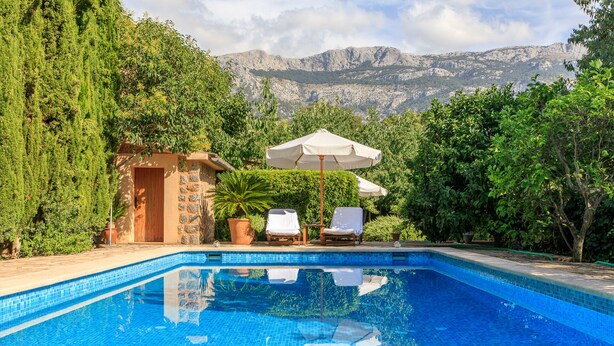 A swimming pool with tiled blue water, surrounded by lush greenery and a mountain backdrop. - Idyllic casita in Soller with garden and pool (Sóller)