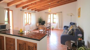 A spacious living area with a kitchen, wooden ceiling beams, a dining table with chairs, a sofa, and a TV. - Idyllic casita in Soller with garden and pool (Sóller)