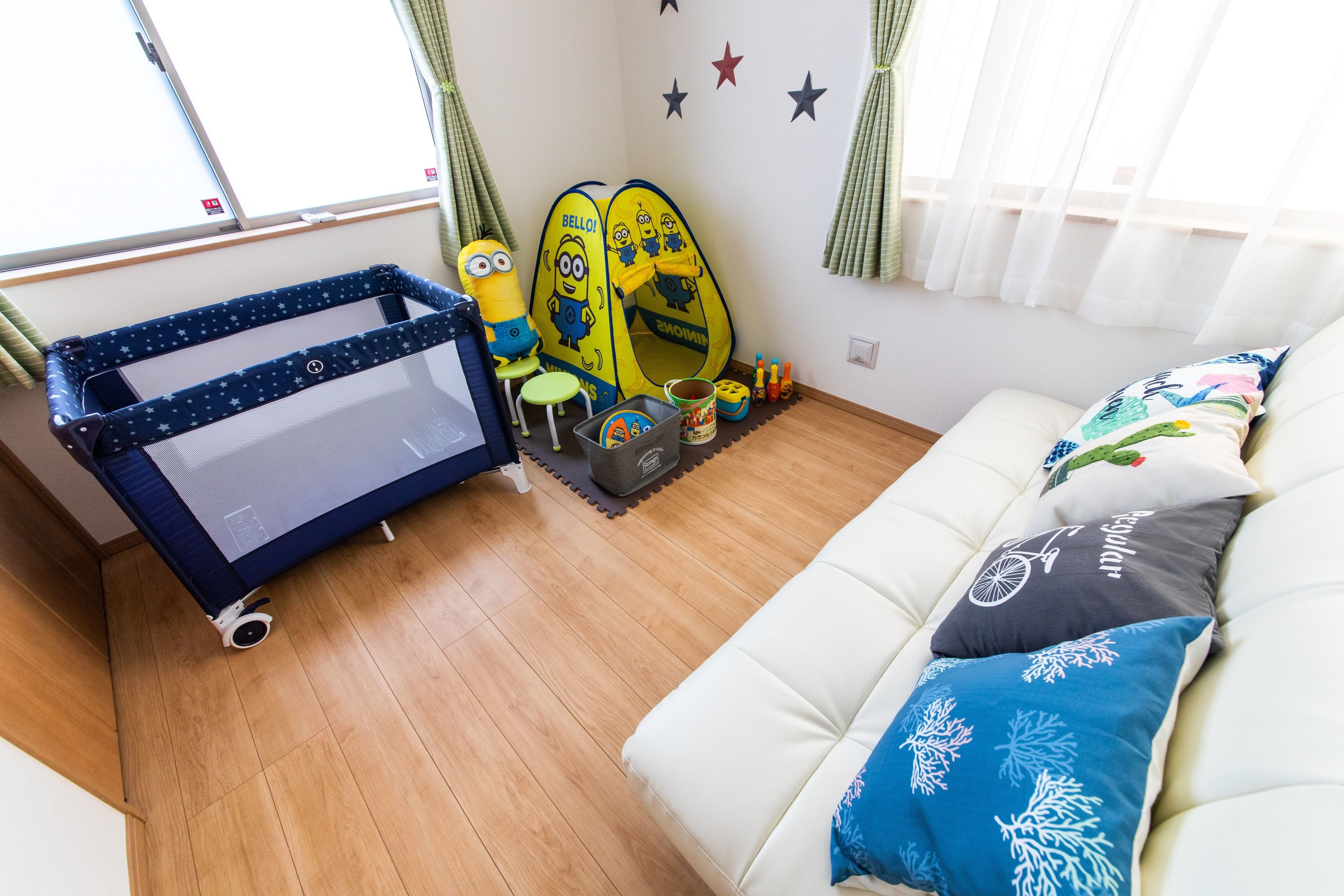 A room with a bed, a sofa, and a play area with toys and a Minion-themed mat.