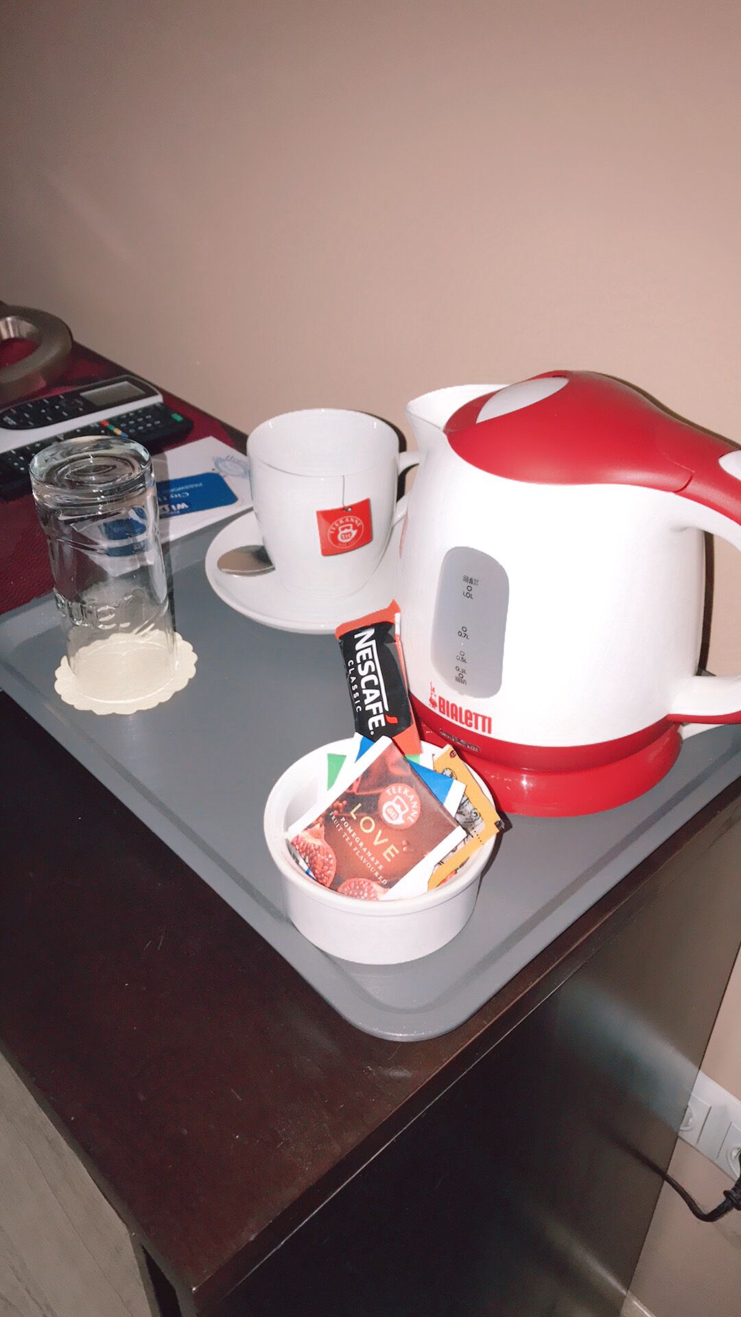 Une machine à café, un verre, une tasse et un petit bol contenant une dosette de café, le tout posé sur une table.
